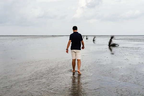Fiatal felnőtt férfi sétál egyedül egy nyugodt és nyugodt strandon apálykor — Stock Fotó