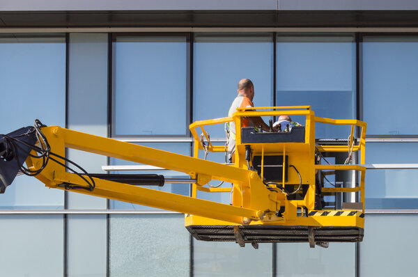 Worker cleaning and repairing curtain wall  from outside mounted on a boom crane truck
