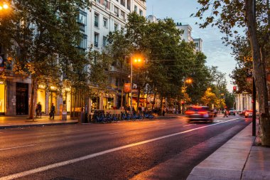 Madrid, İspanya - 3 Ekim 2025: Madrid 'de alacakaranlıkta parlayan mağazalarla Serrano Caddesi' nde trafik ilerliyor