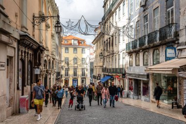 Lizbon, Portekiz - 29 Ekim 2022: Lizbon, Portekiz 'de mimari, dükkanlar ve kaldırım taşı yolda yürüyen insanların yer aldığı hareketli bir sokak manzarası. Carmo Sokağı 'nı yap