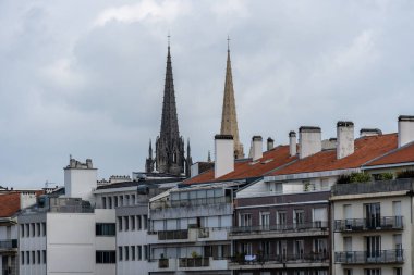 Görüntü, Fransa 'nın Bayonne kentinin mimari güzelliğini yansıtıyor. Bulutlu bir günde şehrin çatılarında yükselen katedralleri gösteriyor..