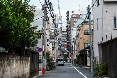 Tokyo, Japonya - 6 Ağustos 2024: Asakusa, Tokyo 'da dar bir cadde, binalar ve elektrik hatlarıyla kaplı, uzakta park edilmiş bir minibüs..