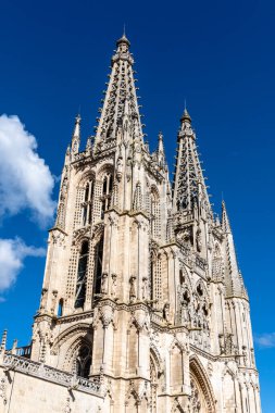 Burgos Katedrali karmaşık Gotik mimari detaylarını sergiliyor, taş duvarlar, kuleler ve parlak gökyüzünün altında uçan payandalar.