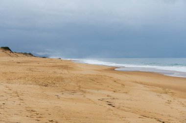 Fotoğraf, kasvetli ve bulutlu bir gökyüzünün altında kıyıya doğru süzülen yumuşak dalgalarla Labenne 'in geniş kumlu plajını yakalar. Sahne bir sükunet hissi uyandırıyor..
