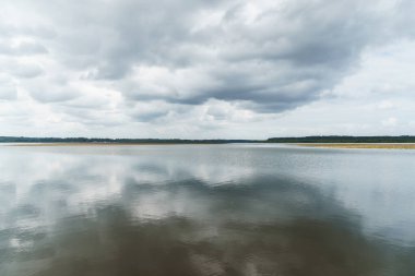 Soustons Gölü dramatik bir gökyüzünü yansıtıyor, yemyeşil kıyı şeritleri ve yüzen su nilüferleri