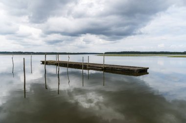 Soustons Gölü sakin su bulutlu bir gökyüzünü ve iki tahta dubayı yansıtıyor.