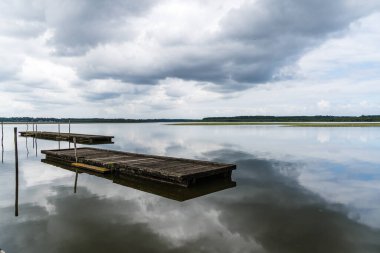 Soustons Gölü sakin su bulutlu bir gökyüzünü ve iki tahta dubayı yansıtıyor.