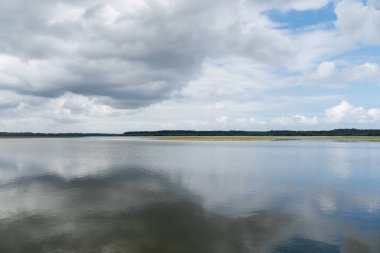 Soustons Gölü dramatik bir gökyüzünü yansıtıyor, yemyeşil kıyı şeritleri ve yüzen su nilüferleri