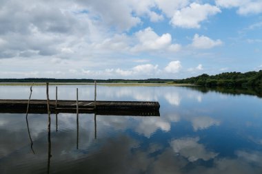 Soustons Gölü sakin su bulutlu bir gökyüzünü ve iki tahta dubayı yansıtıyor.