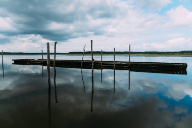 Soustons Gölü sakin su bulutlu bir gökyüzünü ve iki tahta dubayı yansıtıyor.