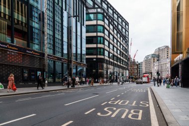 Londra, İngiltere - 27 Ağustos 2023: Bulutlu bir günde modern binalar, yayalar ve kırmızı bir otobüsün yer aldığı hareketli bir sokak sahnesi.