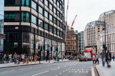 Londra, İngiltere - 27 Ağustos 2023: Bulutlu bir günde modern binalar, yayalar ve kırmızı bir otobüsün yer aldığı hareketli bir sokak sahnesi.