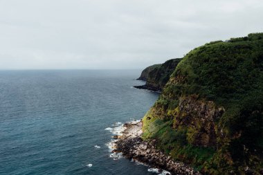 Sao Miguel adası, Azores 'in engebeli kıyı şeridinin manzarası. Bulutlu bir gökyüzünün altında, Atlantik Okyanusu' na ulaşan yemyeşil kayalıklar..