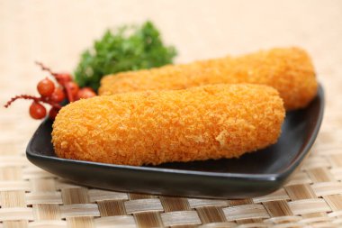 Geleneksel Japon yemeği Korokke ya da Croquette. İki dilim kızarmış patates püresi ya da imo peyniri. Tabakta servis ediliyor ve iki dilim bambudan örülmüş arka planda.
