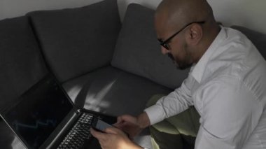 Mobile 'de koltukta dizüstü bilgisayarla ev taraması yapan profesyonel bir erkek. Kilitli, Yüksek Açı