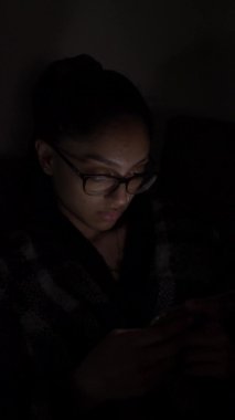 Gözlüklü bir kadının gece cep telefonu izlediği görüntüsü. Dikey Video, Kilitli