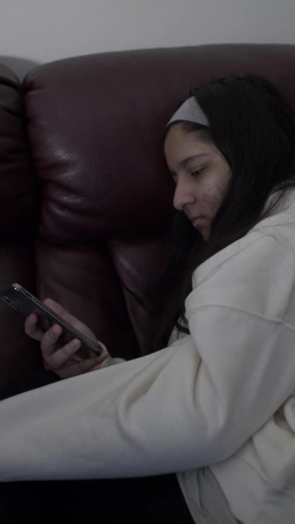 年轻的少女在锁起来的时候用智能手机在沙发上休息 垂直视频 锁定关闭 — 图库视频影像