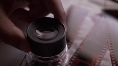 35 mm 'lik fotoğraf negatiflerinin üstünde el ele tutuşan Loupe büyüteç. Kapat, Kapalı