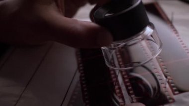 35 mm 'lik fotoğraf negatiflerinin üzerinde el ele tutuşan Loupe Süzülüyor. Kapat, Kapalı