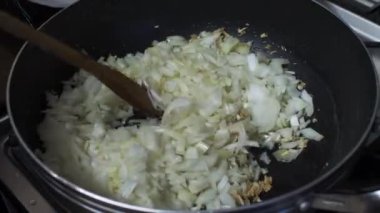 Tavada doğranmış soğan karıştırmak için tahta kaşık kullanıyor. Kilitli 