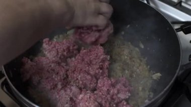 Çiğ kıymayı, soğanlı büyük kızartma tavasına elle yerleştirmek. Kilitli