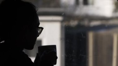 Melankoli Kadını 'nın silueti sıcak bardağı tutup pencereden dışarı bakıyor. Kilitli