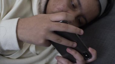 Genç etnik azınlık genci cep telefonuyla koltuğa uzanmış yatıyor. Kilitli