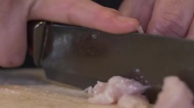 Kesme tahtasında çiğ tavuk eti doğrayan bıçağın yakın çekimi. Kilitli