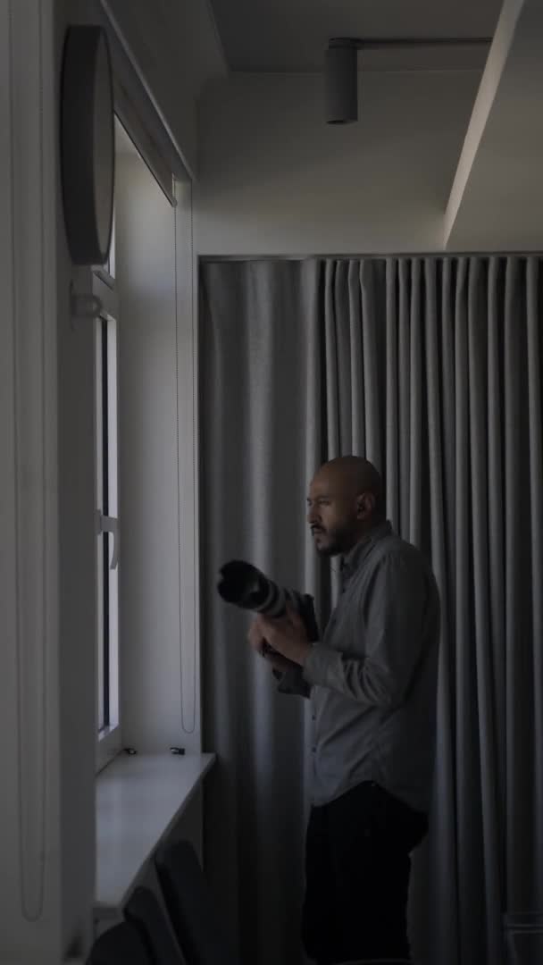 男性探偵カメラで写真を撮るためにウィンドウに向かって歩く 垂直ビデオ ロックオフ — ストック動画