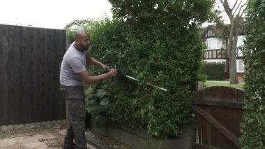 İngiliz Asyalı Yetişkin Erkek Elektirikli Çit Kesme Makinesini Ön Bahçe 'de kullanıyor. Kilitli