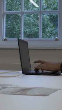 Pencere kenarındaki ofis masasında dizüstü bilgisayarda yazan etnik azınlık erkek ofisi. Dikey Video, Kilitli