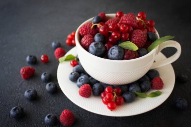 Siyah arka planda çay fincanındaki nane yapraklı farklı meyveler..