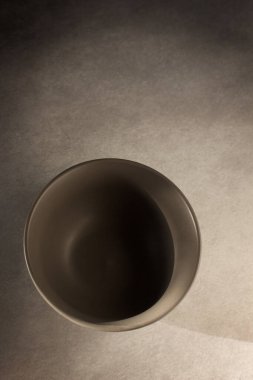 Doğal ışık tarafından aydınlatılan boş gri seramik kâse koyu gri bir arkaplan üzerinde yaratıcı gölgeler oluşturmuştur. Ürün sunumu, yerleşimi, şablonu için alanı kopyala.