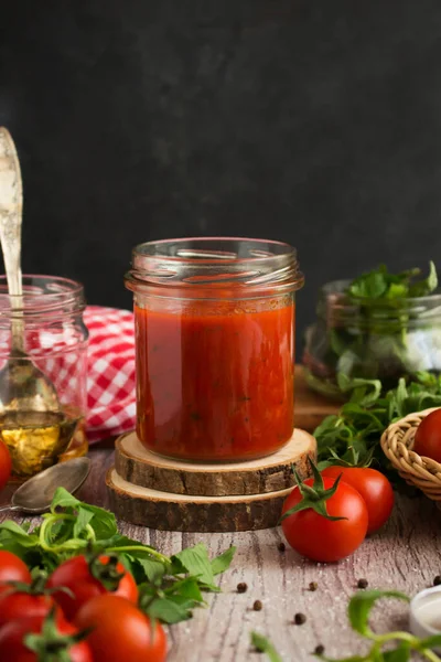 Classic homemade tomato sauce for pasta and pizza in a glass jar on a board. Composition with herbs, spices, oil and tomatoes on a wooden background for overlay on product presentation, template, posters, photo and wallpapers.