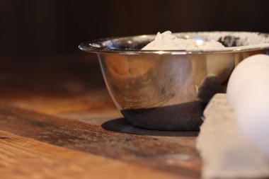 Tahta bir masanın üzerinde birkaç beyaz yumurta ve içinde beyaz un bulunan metal kaplar.