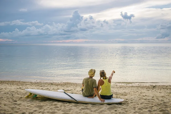 Happy couple with paddle board on the beach at sunset — Stock Photo, Image