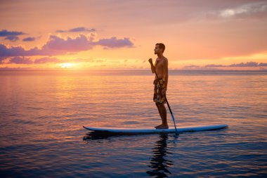 Adam paddleboarding gün batımında silüeti