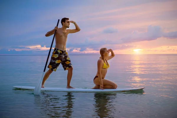 Pareja feliz surfeando juntos en la tabla de paddle al atardecer — Foto de Stock