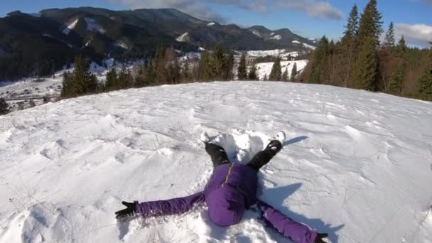 Счастливая женщина делает снежного ангела в зимней горе — стоковое видео