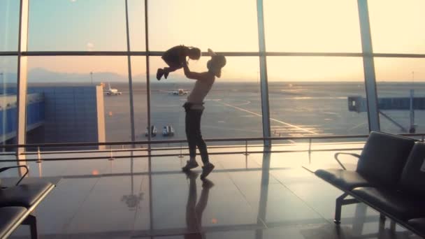 Gelukkige vrouw met kind in de luchthaven met opgeheven handen bij zonsondergang — Stockvideo