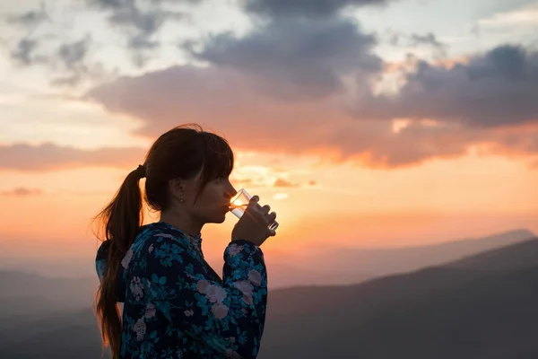 Жінка п'є воду на фоні заходу сонця — стокове фото