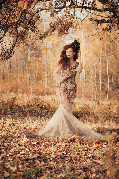 Beautiful elegant woman standing in the autumn forest in chiffon dress with yellow autumn leaves
