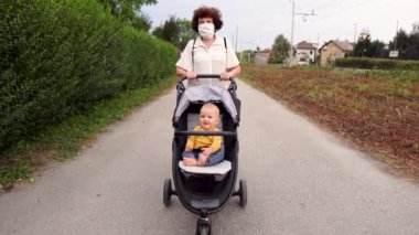 Bebek arabasını iten tıbbi maskeli bir kadın. Covid-19, koronavirüs güvenlik önlemleri. 4K