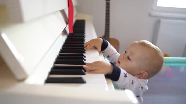 Un mignon petit garçon essayant de jouer d'un grand piano tout en se levant. 4K — Video