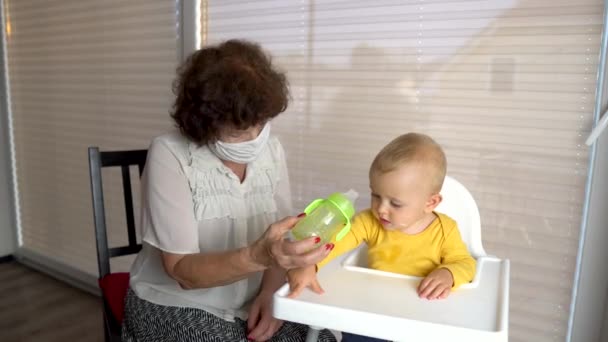 Kobieta chroniona maską medyczną, dająca dziecku wodę w domu. Kowid-19. — Wideo stockowe