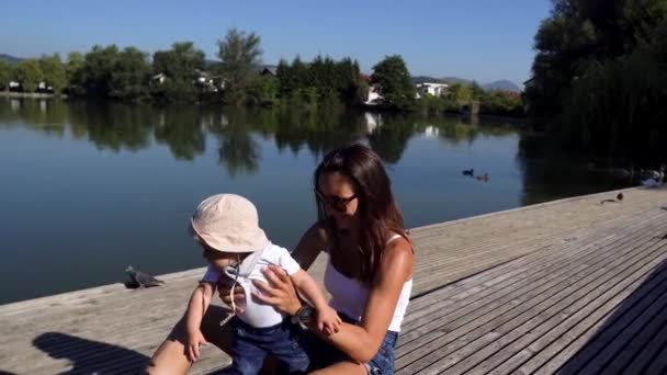 귀여운 사내 아이와 그의 어머니가 멋진 호수의 나무 부둣가에서 오리를 보고 있는 모습 — 비디오