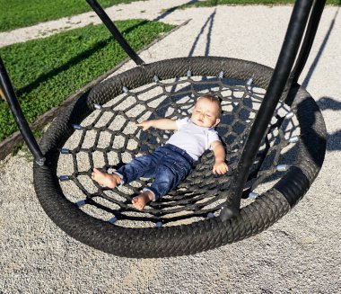 Güneşli bir günde gözleri kapalı salıncakta sallanan sevimli bir oğlan.