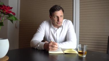 Ağlayan bir adam aşk mektubu yazıyor ve viski içiyor.