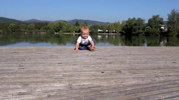 Ein niedlicher kleiner Junge lernt an einem sonnigen Tag an einem See, in die Kamera zu kriechen. 4K — Stockvideo