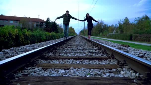Una pareja camina por las vías del tren tomados de la mano — Vídeo de stock
